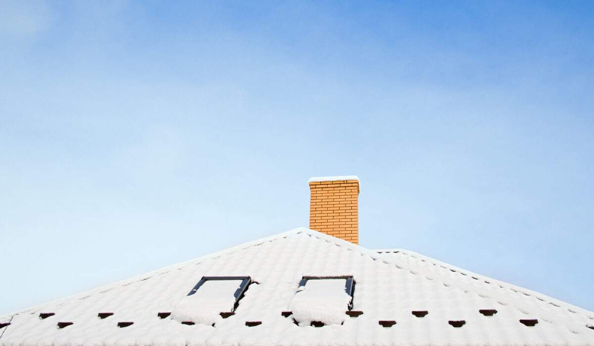 Closeup of asphalt roof covered in snow showing roof ventilation and chimney that help prevent ice dams.